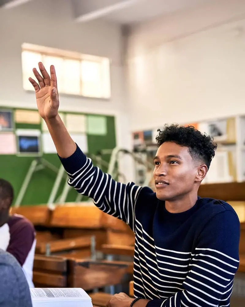 A young man in a classroom raising his hand
