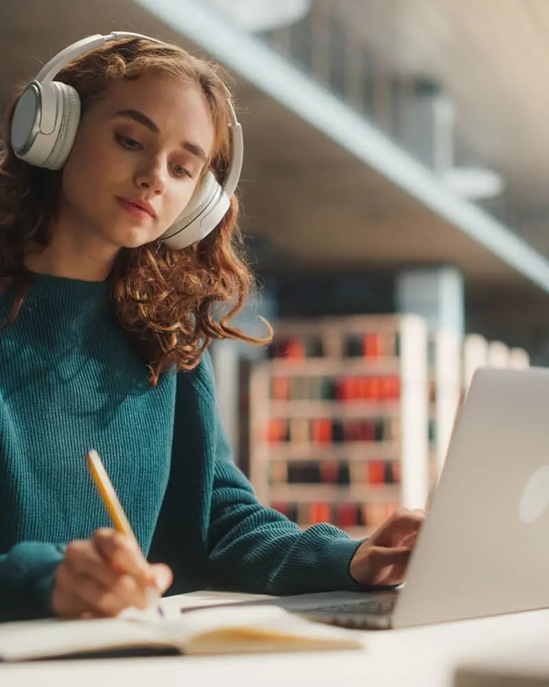 A girl with headphones on writing in a notebook